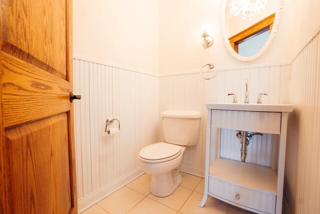 half bathroom featuring a wainscoted wall, toilet, and tile patterned flooring