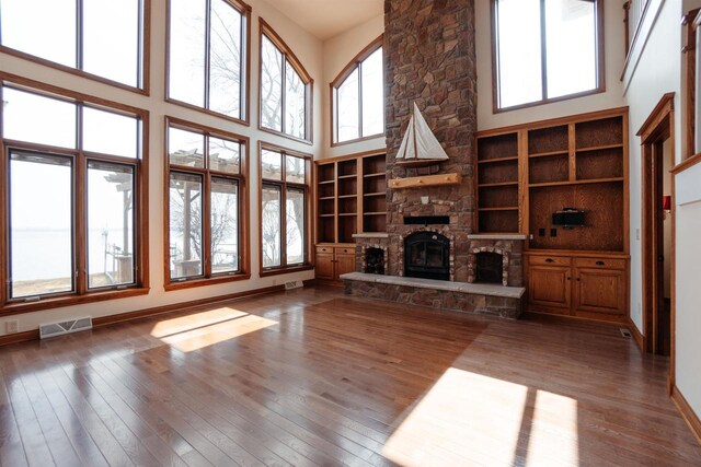 unfurnished living room featuring hardwood / wood-style flooring, a towering ceiling, a stone fireplace, and visible vents