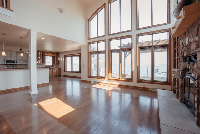 unfurnished living room with dark wood-type flooring, baseboards, decorative columns, and a stone fireplace