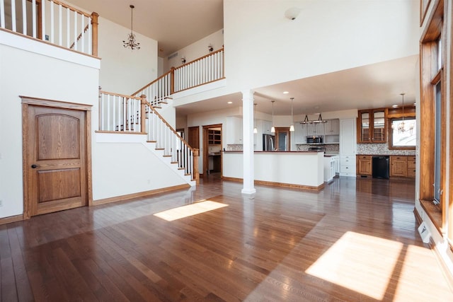 unfurnished living room with baseboards, dark wood-style flooring, decorative columns, stairs, and a towering ceiling