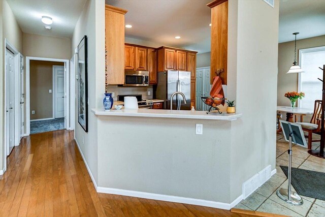 kitchen featuring brown cabinets, appliances with stainless steel finishes, visible vents, light countertops, and baseboards