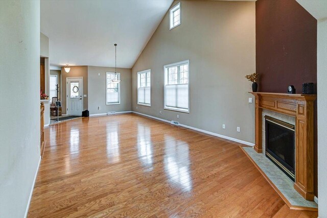 unfurnished living room featuring a fireplace, high vaulted ceiling, baseboards, and light wood-style floors