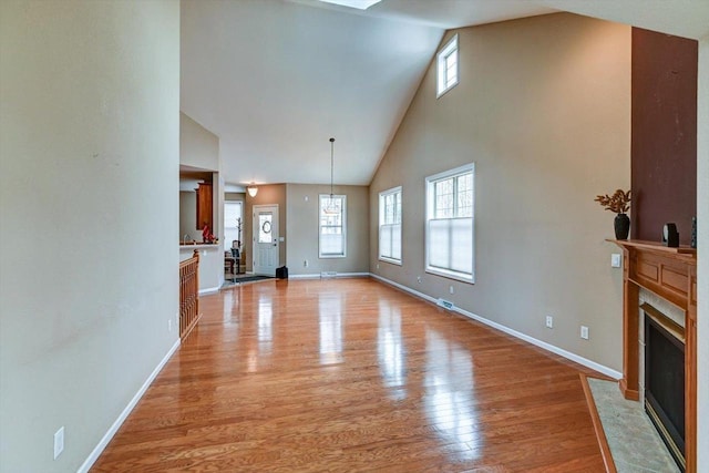 unfurnished living room featuring light wood-type flooring, high vaulted ceiling, a wealth of natural light, and a fireplace with flush hearth