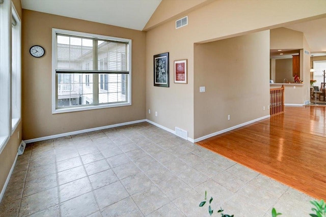 tiled spare room with baseboards, visible vents, and vaulted ceiling