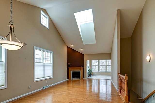 unfurnished living room featuring visible vents, baseboards, a fireplace, wood finished floors, and a skylight