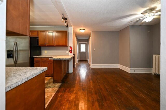 301 Summit St, Spooner, WI 54801 - kitchen with light countertops, radiator heating unit, stainless steel fridge, brown cabinets, and dark wood-style flooring