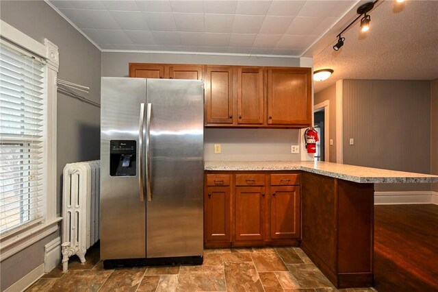 301 Summit St, Spooner, WI 54801 - kitchen with light countertops, a peninsula, radiator heating unit, stainless steel refrigerator with ice dispenser, and brown cabinetry