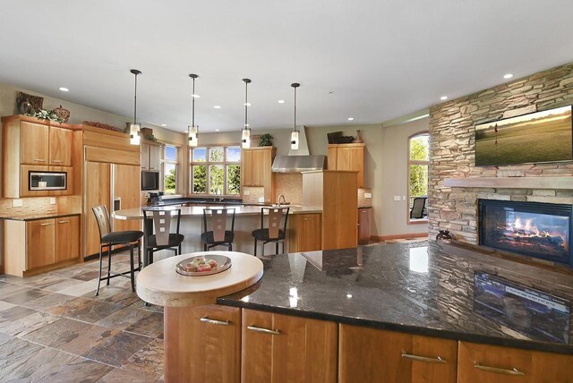 7548 Fallen Oak Dr, Verona, WI 53593 - kitchen featuring built in appliances, tasteful backsplash, a stone fireplace, a large island, and wall chimney range hood