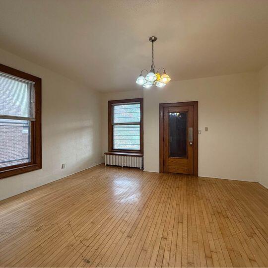 3034 W State St Unit 3036, Milwaukee, WI 53208 - empty room featuring radiator heating unit, light wood-style flooring, and an inviting chandelier