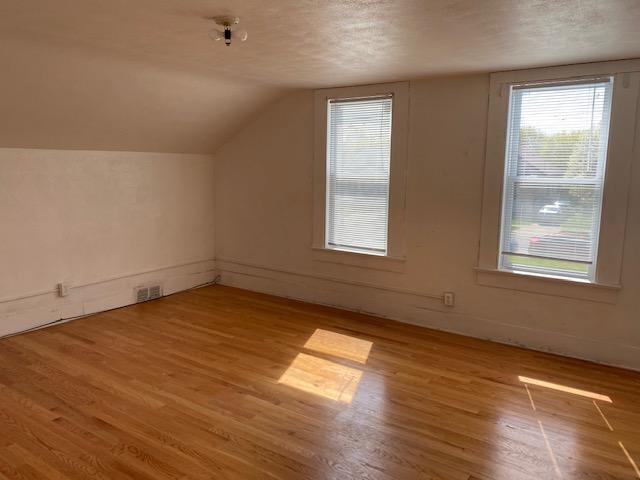 additional living space with lofted ceiling, a textured ceiling, visible vents, and light wood-type flooring