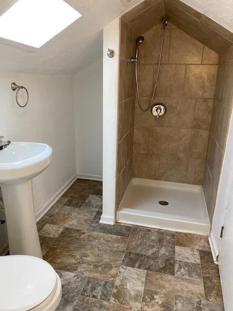 full bath with baseboards, stone finish floor, toilet, and a stall shower