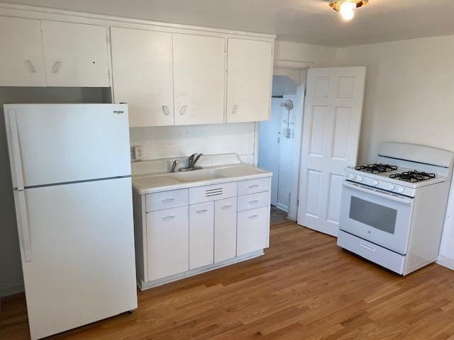 kitchen with light wood-type flooring, light countertops, a sink, and white appliances