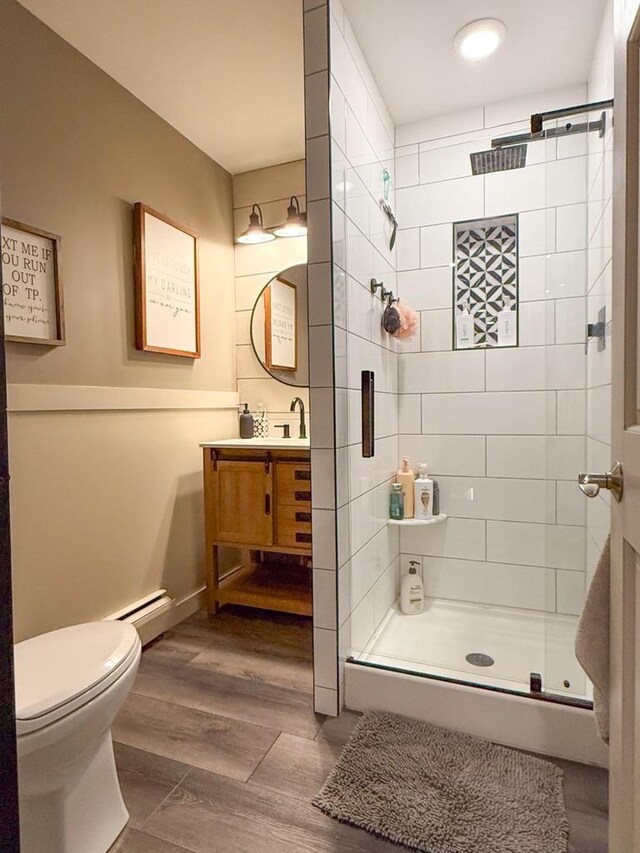 bathroom featuring wood finished floors, toilet, baseboard heating, vanity, and a stall shower