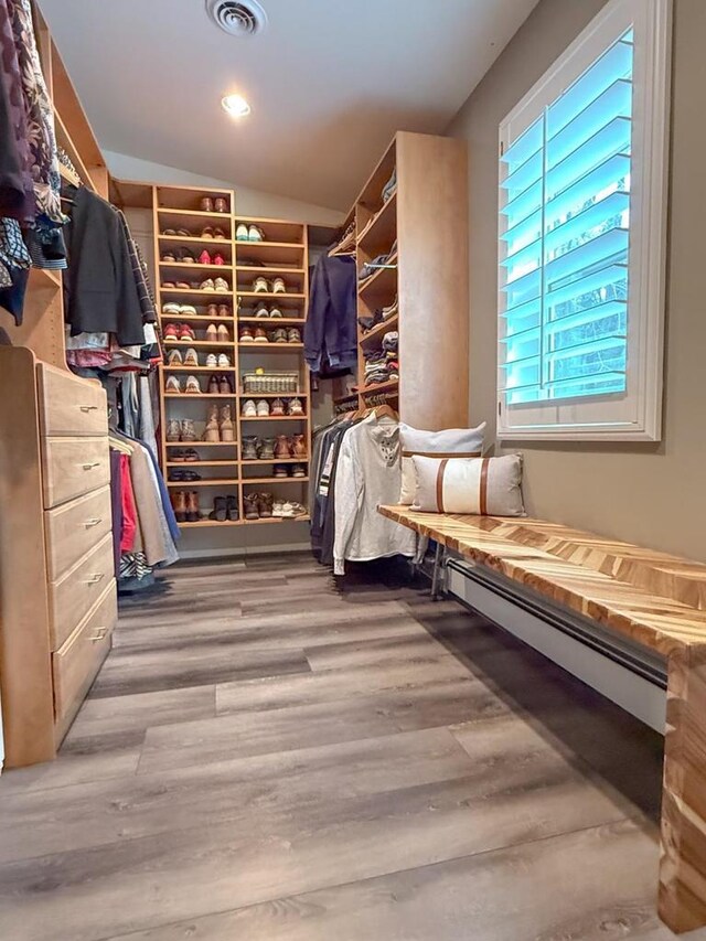 spacious closet with visible vents, baseboard heating, lofted ceiling, and wood finished floors