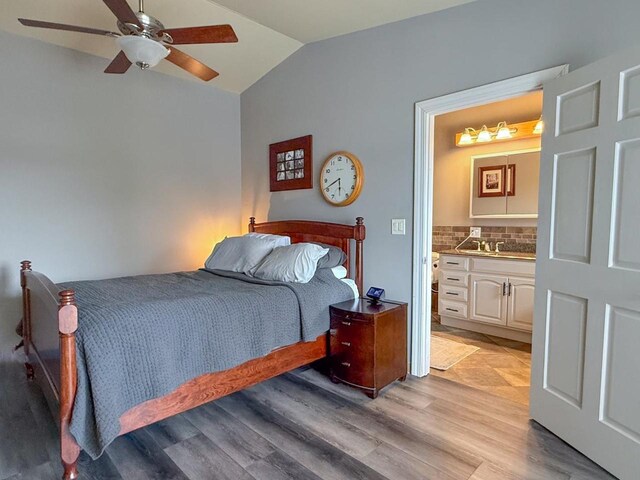 bedroom featuring connected bathroom, vaulted ceiling, light wood-style floors, and a ceiling fan