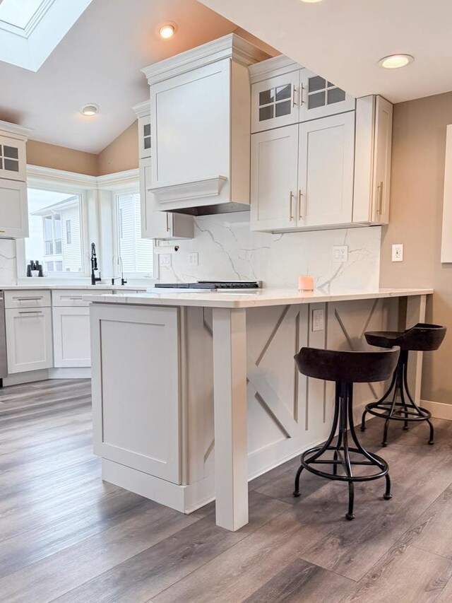 kitchen with a kitchen breakfast bar, light countertops, decorative backsplash, vaulted ceiling with skylight, and light wood-style floors