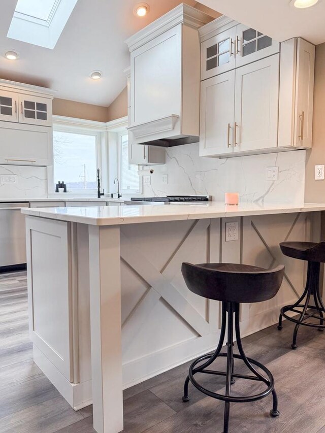 kitchen with light countertops, dishwasher, vaulted ceiling with skylight, glass insert cabinets, and a breakfast bar area