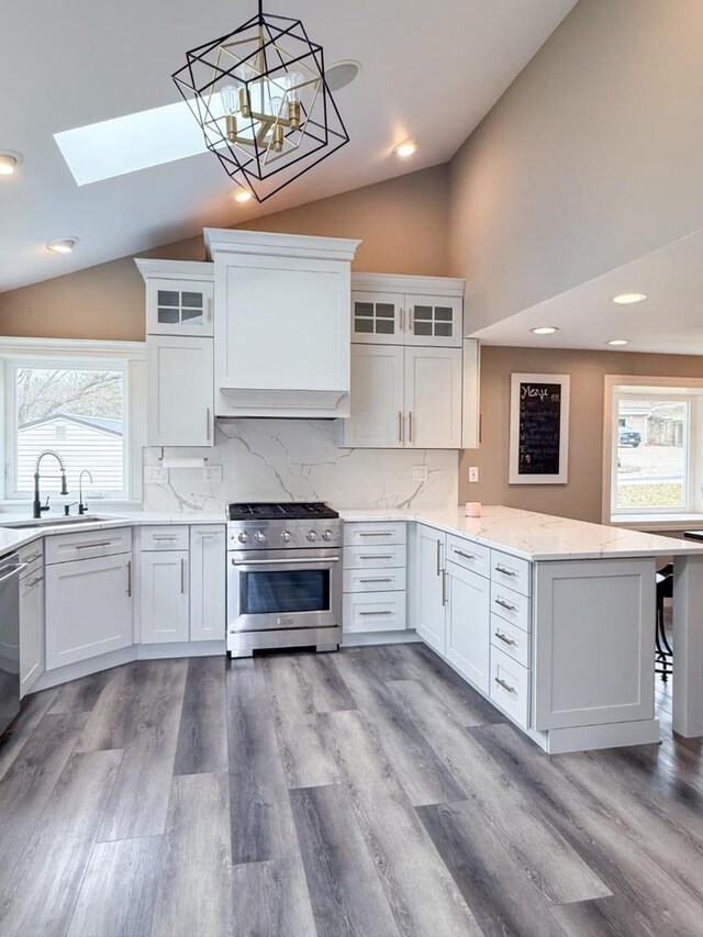 kitchen with high end stove, a sink, vaulted ceiling with skylight, white cabinets, and a peninsula
