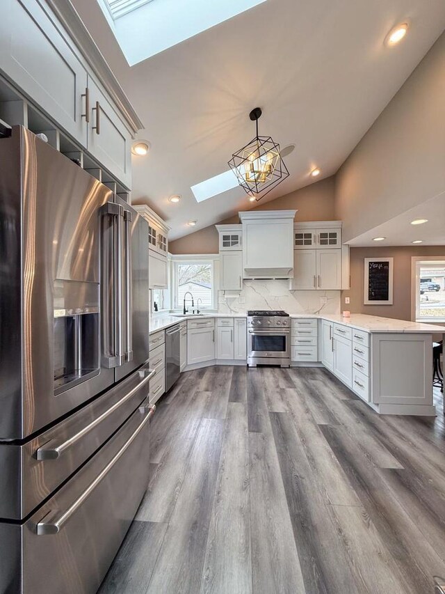 kitchen with a peninsula, appliances with stainless steel finishes, glass insert cabinets, a sink, and lofted ceiling with skylight