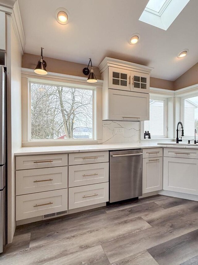 kitchen with light countertops, a sink, light wood finished floors, appliances with stainless steel finishes, and lofted ceiling with skylight