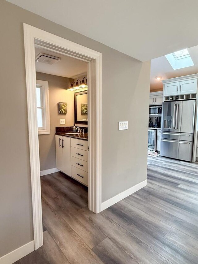 hallway with dark wood-style flooring, baseboards, a sink, a skylight, and visible vents