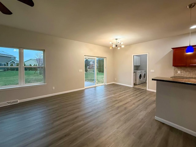 2208 W Milwaukee St, Stoughton, WI 53589 - unfurnished living room with separate washer and dryer, dark wood-style floors, baseboards, ceiling fan with notable chandelier, and visible vents