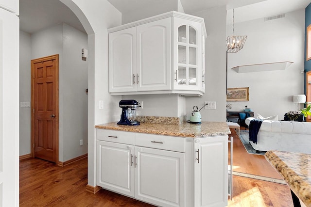 kitchen featuring glass insert cabinets, arched walkways, white cabinetry, visible vents, and wood finished floors