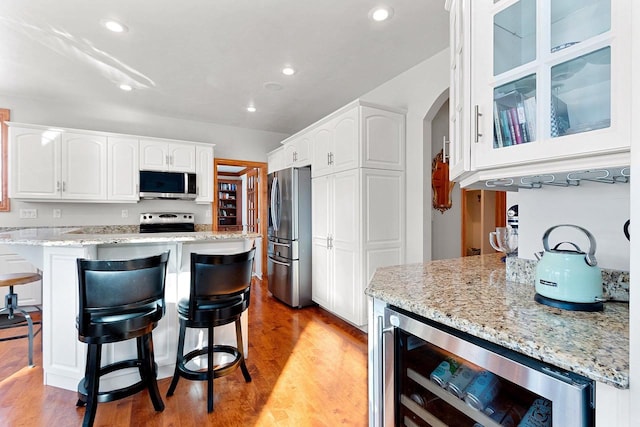 kitchen featuring light stone countertops, white cabinets, a breakfast bar, beverage cooler, and stainless steel appliances