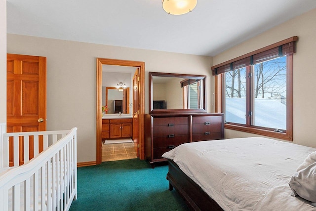 bedroom with a sink, dark carpet, baseboards, and ensuite bathroom
