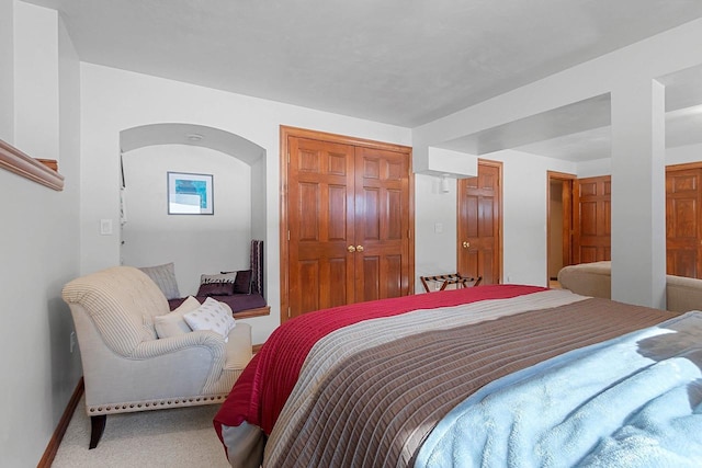 bedroom with carpet floors, baseboards, arched walkways, and a closet