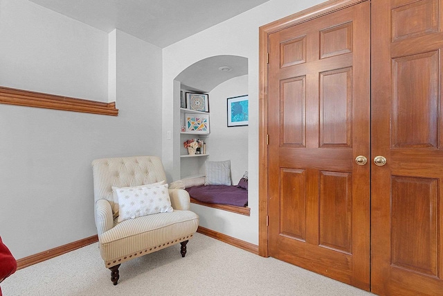 sitting room with arched walkways, carpet flooring, baseboards, and built in shelves