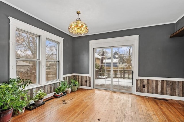 unfurnished dining area with hardwood / wood-style floors, a wainscoted wall, crown molding, and a healthy amount of sunlight