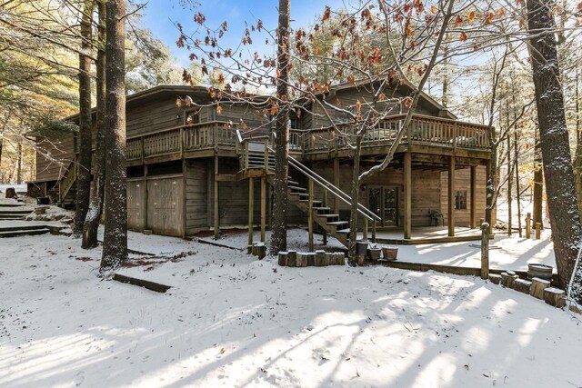 snow covered back of property featuring a deck and stairway