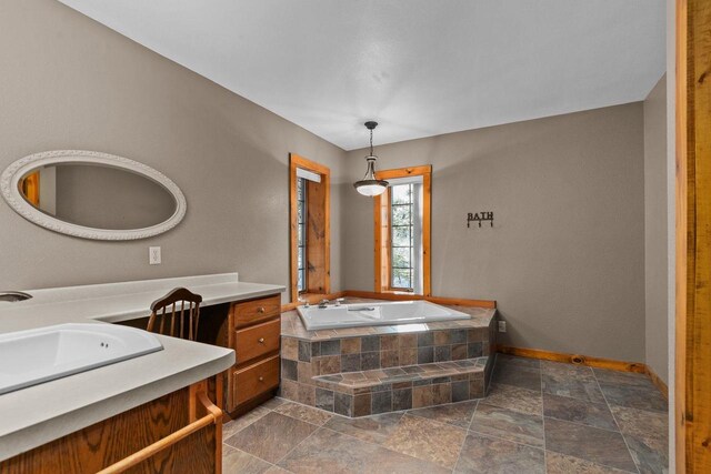 full bath featuring baseboards, a bath, vanity, and stone tile flooring
