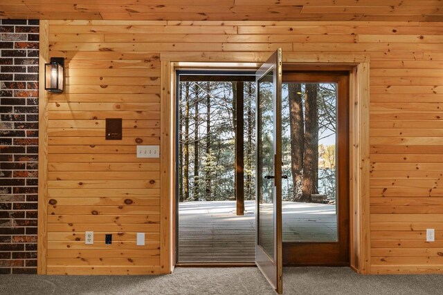 doorway to outside with carpet floors and wooden walls
