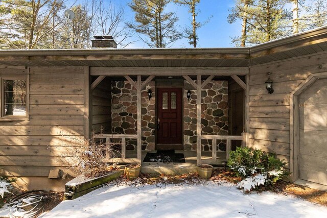 view of exterior entry with stone siding and a chimney