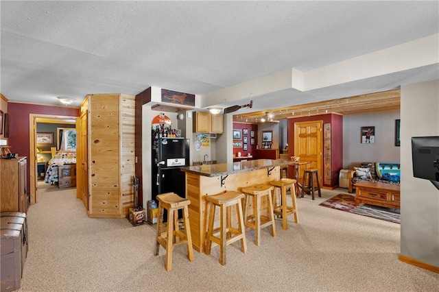 6825 W Lakewood Blvd, Ladysmith, WI 54848 - kitchen featuring a textured ceiling, a kitchen breakfast bar, black fridge, a center island, and light colored carpet