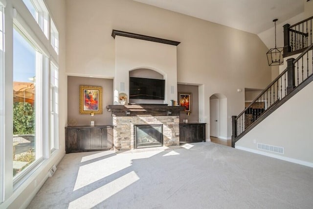 carpeted living room featuring a stone fireplace, high vaulted ceiling, stairs, and visible vents