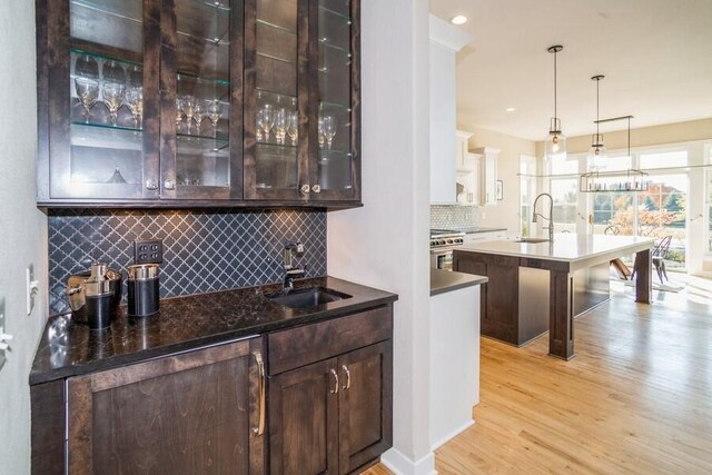 bar featuring hanging light fixtures, light wood-type flooring, high end stove, and a sink