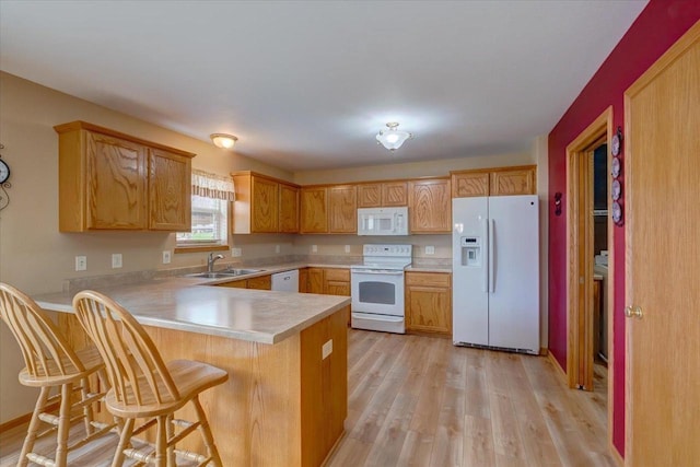 kitchen featuring light countertops, a sink, a peninsula, white appliances, and light wood-style flooring