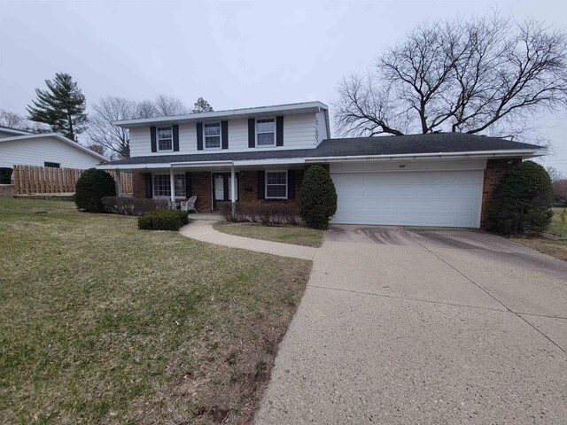 302 Riverview Ct, Portage, WI 53901 - traditional-style house featuring a front yard, concrete driveway, fence, an attached garage, and brick siding