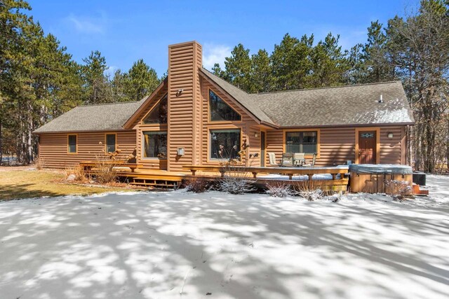 rear view of house featuring a hot tub, a deck, central AC, a chimney, and a shingled roof