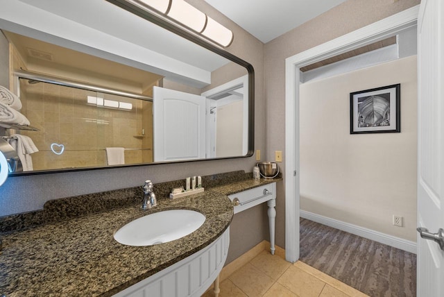 bathroom with tile patterned floors, a tile shower, vanity, and baseboards