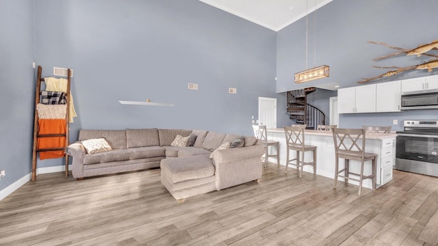 living area with stairs, light wood finished floors, baseboards, a towering ceiling, and ornamental molding