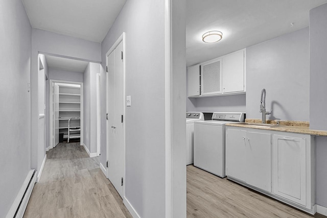 washroom with a sink, light wood-type flooring, baseboard heating, independent washer and dryer, and cabinet space