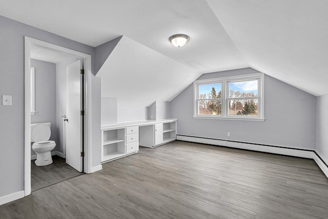additional living space with a baseboard radiator, baseboards, vaulted ceiling, and wood finished floors