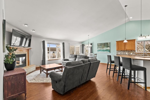 living room with dark wood-style flooring, an inviting chandelier, a tile fireplace, and lofted ceiling