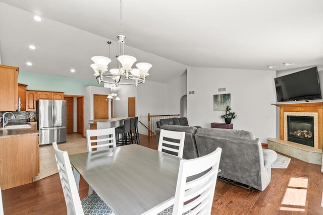 dining room with wood finished floors, an inviting chandelier, a glass covered fireplace, and lofted ceiling