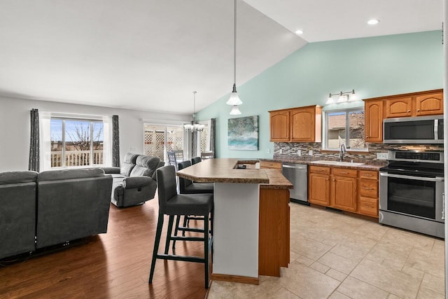 kitchen with a kitchen breakfast bar, a kitchen island, a sink, stainless steel appliances, and a notable chandelier