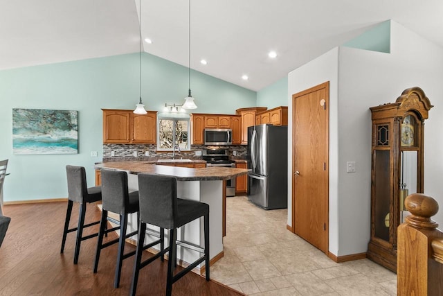 kitchen featuring tasteful backsplash, dark countertops, brown cabinets, a breakfast bar area, and stainless steel appliances